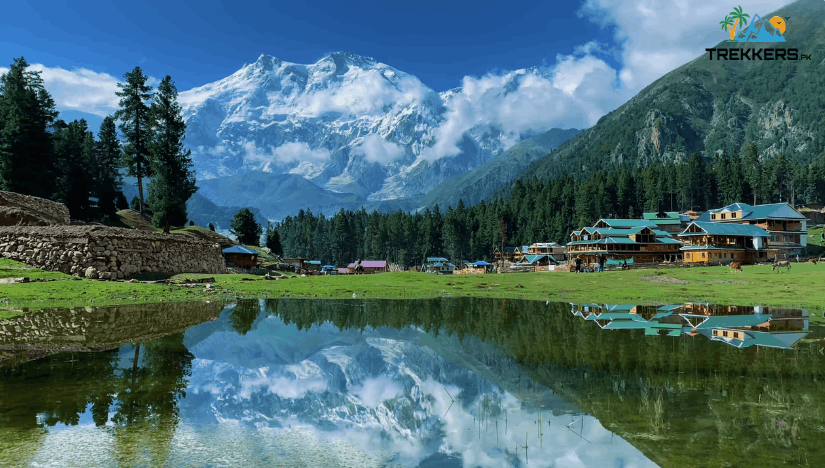 The iconic crystal clear reflection lake at Fairy Meadows in Pakistan showcasing the snow-covered north face of Nanga Parbat mountain with traditional wooden resorts.