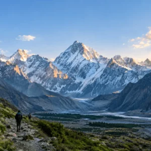 A sweeping panoramic landscape showing trekkers hiking a trail through a valley toward snow-covered high peaks including K2 at sunset, located in the Concordia region of Pakistan. Best Mountains to Visit in Pakistan