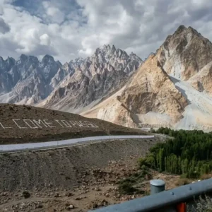 Scenic view of the iconic Welcome to Passu signboard along the highway with the sharp peaks of Passu Cones in Hunza Valley in the background.