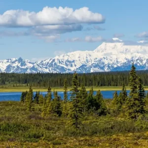 Snow-covered peaks of Denali and the Alaska Range rising above evergreen boreal forests and blue alpine lakes in the USA.